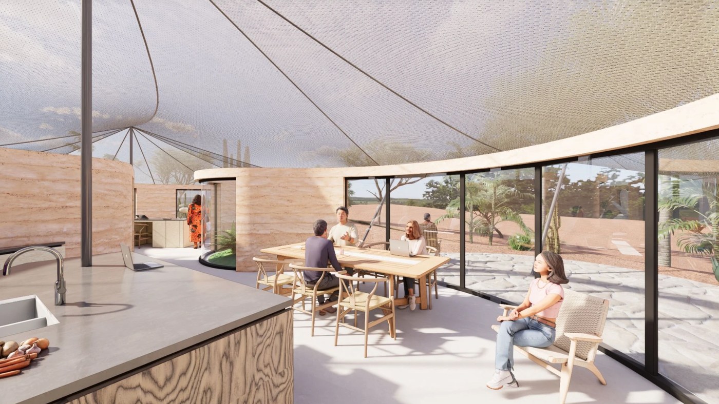 Guests gathered at the dining table inside the common room, curved glass opening to the desert garden